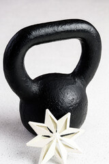 Fototapeta na wymiar Kettlebell winter fitness, black kettlebell on a white background with silver sparkles and a white snowflake 