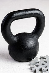 Fototapeta na wymiar Kettlebell winter fitness, black kettlebell on a white background with silver sparkles and a silver snowflake 