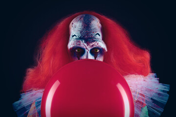 Terrifying clown with red air balloon on black background. Halloween party costume