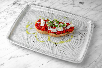 Bruschetta with baked peppers and tomatoes in a festive plate on a marble background. Restaurant banquet menu.