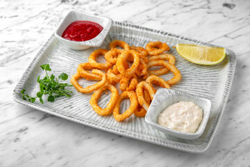 Onion or squid rings with sauce in a festive plate on a marble background. Restaurant banquet menu.