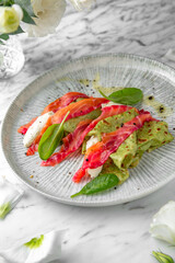 Spinach pancakes with salmon, colored beets in a festive plate on a marble background. Restaurant banquet menu.