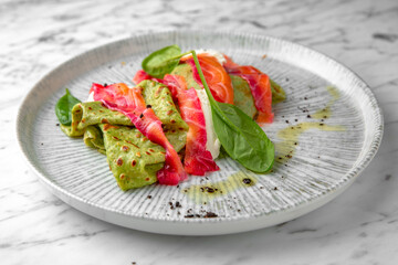 Spinach pancakes with salmon, colored beets in a festive plate on a marble background. Restaurant banquet menu.
