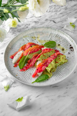 Spinach pancakes with salmon, colored beets in a festive plate on a marble background. Restaurant banquet menu.