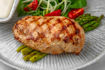 Whole grilled chicken breast, asparagus and tomato salad with arugula in a festive plate on a marble background. Restaurant banquet menu.