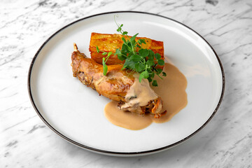 Baked rabbit leg with pumpkin pie in a festive plate on a marble background. Restaurant banquet menu.