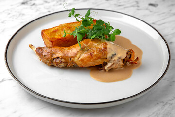 Baked rabbit leg with pumpkin pie in a festive plate on a marble background. Restaurant banquet menu.