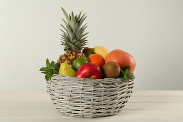 Fresh ripe fruits in wicker bowl on white wooden table