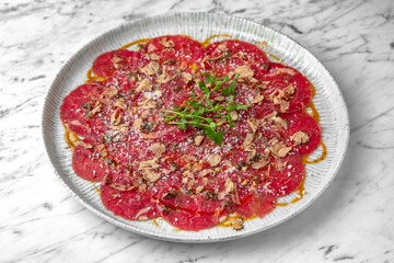 Beef carpaccio in a festive plate on a marble background. Restaurant banquet menu.
