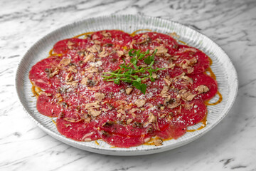 Beef carpaccio in a festive plate on a marble background. Restaurant banquet menu.
