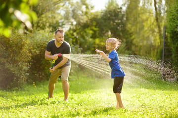 Funny little boy with his father playing with garden hose in sunny backyard. Preschooler child...