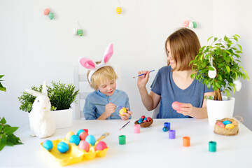 Fototapeta na wymiar Young mother and her son are painting eggs for Easter. Child wearing funny bunny ears. Happy family preparing for Easter.