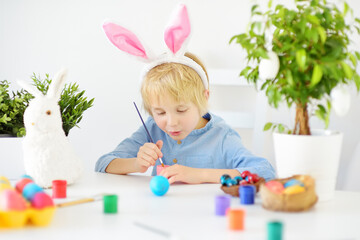 Cute boy paints eggs for Easter holiday. Preparing for celebration is a joy for kids.