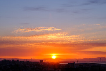 早朝、日が昇りあたりはオレンジ色に染まる。雲に隠れていた太陽が顔を出す。大阪湾の先に和泉山脈・紀伊山地の稜線が見える。