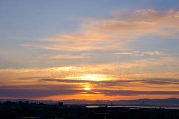 早朝、日が昇りあたりはオレンジ色に染まる。雲に隠れていた太陽が顔を出す。大阪湾の先に和泉山脈・紀伊山地の稜線が見える。