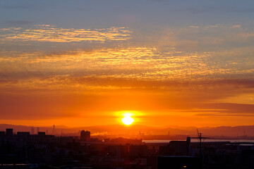 早朝、日が昇りあたりはオレンジ色に染まる。雲に隠れていた太陽が顔を出す。大阪湾の先に和泉山脈・紀伊山地の稜線が見える。