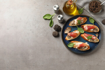 Fototapeta Delicious bruschettas with cheese, prosciutto and slices of black truffle on grey table, flat lay. Space for text obraz