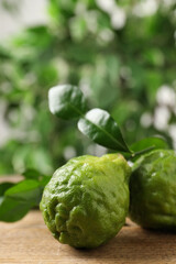 Fototapeta premium Fresh ripe bergamot fruits with green leaves on wooden table against blurred background, closeup. Space for text