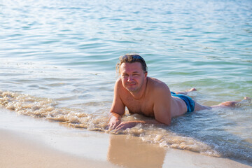 the guy on the beach in swimming trunks lies in the water