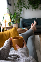 POV of young woman relaxing at home with cup of tea lying on sofa. Vertical. - obrazy, fototapety, plakaty