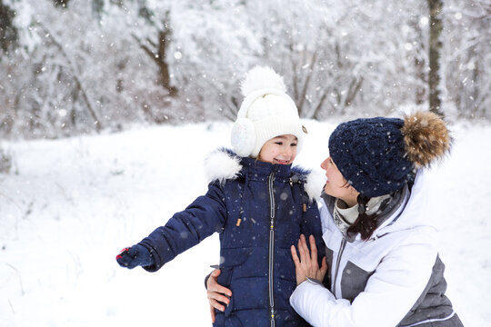 Mom and daughter hugging, looking at each other with love, on a walk. Winter entertainment outside, active recreation, fun in the cold in warm clothes. Outdoor recreation, fun childhood, strong family