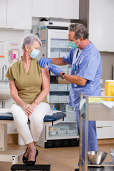 A White Male Medical Nurse Administering a Covid-19 Vaccine with a Syringe Needle to an Elderly...