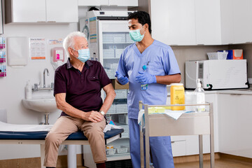 A Young Indian Male Medical Nurse Consults with an Elderly Senior Male Patient about Covid-19...