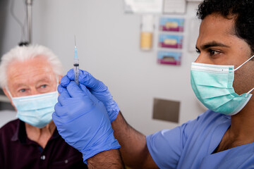A Young Indian Male Medical Nurse Administering a Covid-19 Vaccine with a Syringe Needle to an...