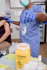 A Young Indian Male Nurse Disposes of Syringe Needle Safely in Sharps Collector after a Covid-19...