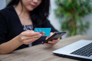 Young woman holding cell phone and credit card in front of laptop