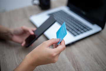 Woman hand holding cell phone and credit card in front laptop