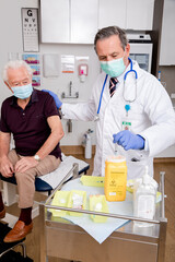 A White Male Medical Doctor Disposes of Syringe Needle Safely in Sharps Collector after a Covid-19 Vaccine Injection Wearing Generic ID Badge, Lab Coat, Gloves and Mask in Hospital or Health Clinic. 