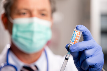 A White Male Medical Doctor Extracting a Covid-19 Vaccine with a Syringe Needle Wearing Generic ID...