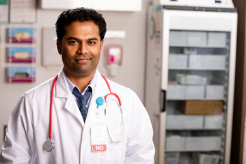 A Portrait of an Young Indian Male Medical Doctor with Generic ID Badge wearing a Lab Coat and...