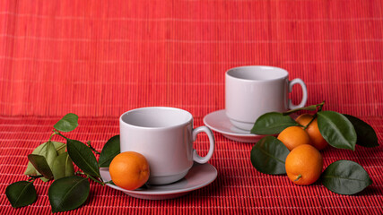 Two empty cups with saucers and the tangerines with green leaves on red background. Copy space.
