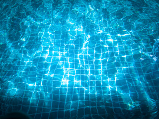 Blue swimming pool water, with waves, and reflections from sunlight, with dark shadows at the bottom of the image, late in the holidays.