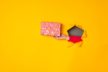 Santa's hand holding a box with a gift in the hole yellow background