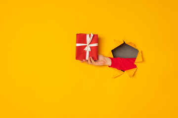 Santa's hand holding a box with a gift in the hole yellow background