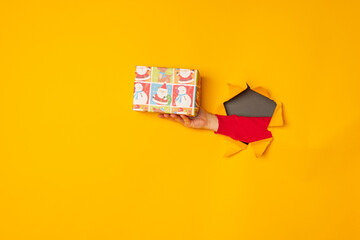 Santa's hand holding a box with a gift in the hole yellow background