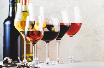 Red, rose and white wine glasses set on gray table background. Wine tasting. Hard light and harsh shadows
