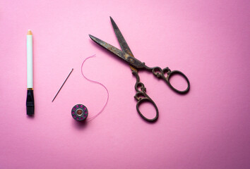 bobbin or spool of thread and scissors with needle for sewing on pink background , hobbies and pastimes , minimalist image .