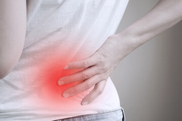 woman in white t-shirt touch her waist and hold lower back with red spot area which suffering from back pain or back ache