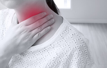 black and white photo of asian woman in white t-shirt touch and hold her neck with hand because of sore throat and illness symptom showing in red spot area