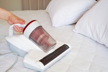 woman hand hold handheld vacuum cleaner  to clean white  bed sheet , pillows and bed set to remove stain , dust , pet hair and dust mites to prevent symptom of allergic to dust