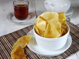 Keripik sukun is chips which made of deep fried thin slice breadfruit.  Crispy savory snack. Typical Indonesian traditional chips. Easy to find as street food. Serving in white bowl along with tea. 