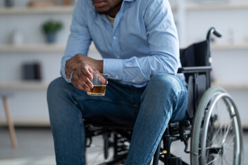 Cropped view of handicapped black guy in wheelchair drinking whiskey at home. Disability depression...