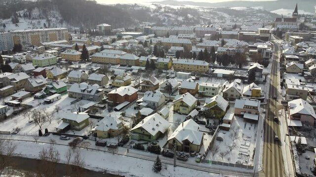 Aerial drone footage flying overlooking housing estates, public parks and commercial properties in a built up area in the small town of Bardejov in Slovakia during winter snowy sunrise, river Topla