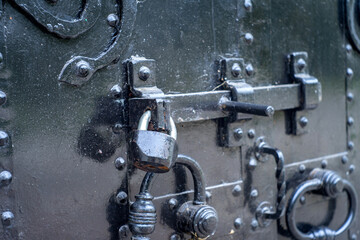 The metal gate is padlocked. Rusty padlock on the gate, close-up. Rough iron doors.