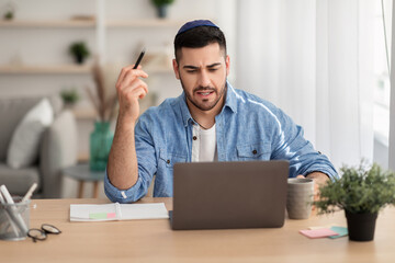 Focused israeli man working on laptop amd writing at home