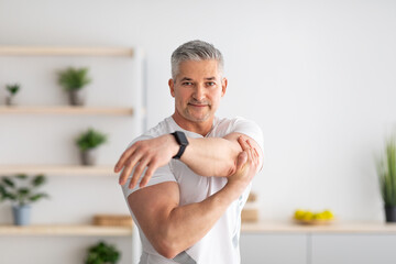 Obraz premium Morning training. Active mature man warming up, stretching hands at home, training in living room interior